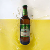 Wijnhandel Alexander Skopsko lager bier in een 0,33L fles met groen etiket, omringd door spatten van goudgeel bier.